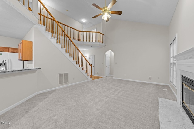 unfurnished living room featuring high vaulted ceiling, ceiling fan, arched walkways, stairway, and a fireplace