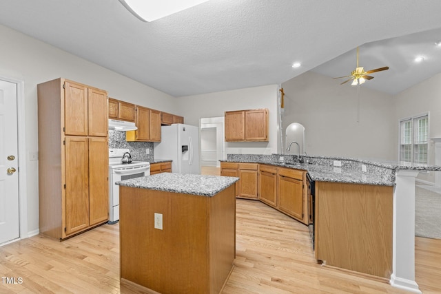 kitchen with white appliances, a peninsula, under cabinet range hood, light wood-type flooring, and a textured ceiling