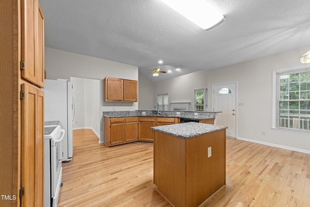 kitchen with white appliances, a peninsula, a textured ceiling, light wood finished floors, and brown cabinetry