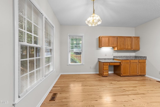 kitchen featuring brown cabinetry, light wood-style flooring, pendant lighting, and baseboards