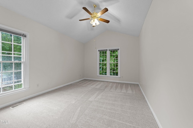 empty room featuring plenty of natural light, light colored carpet, a ceiling fan, and vaulted ceiling