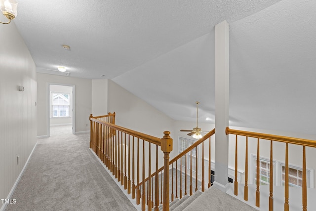 hall featuring an upstairs landing, a textured ceiling, carpet, baseboards, and lofted ceiling