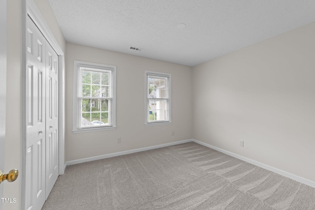 unfurnished bedroom featuring light colored carpet, a textured ceiling, baseboards, and a closet