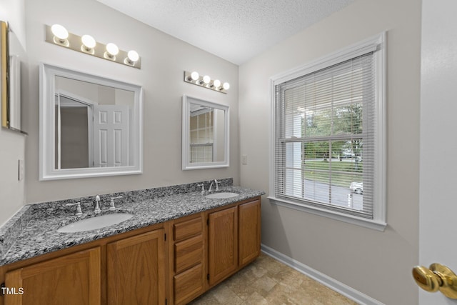 bathroom with baseboards, double vanity, and a textured ceiling