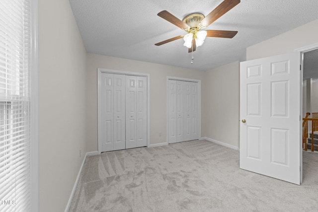 unfurnished bedroom with carpet flooring, two closets, baseboards, a textured ceiling, and ceiling fan