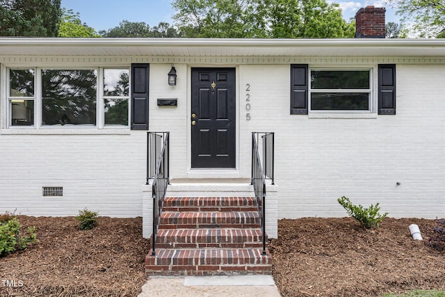 property entrance featuring a chimney, brick siding, and crawl space