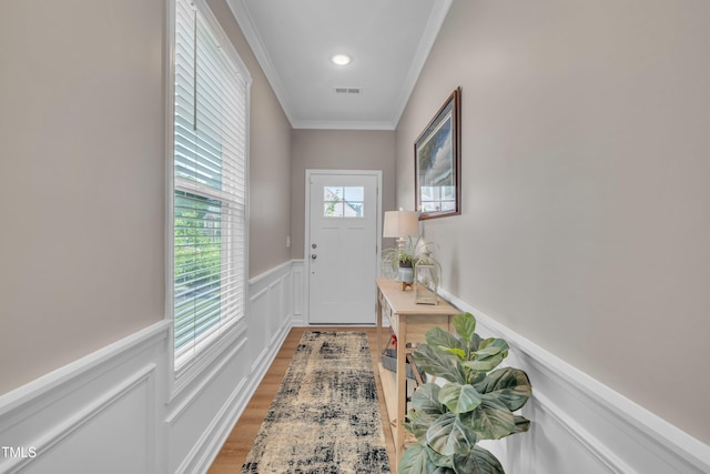 doorway with crown molding, a wainscoted wall, light wood-type flooring, and a decorative wall