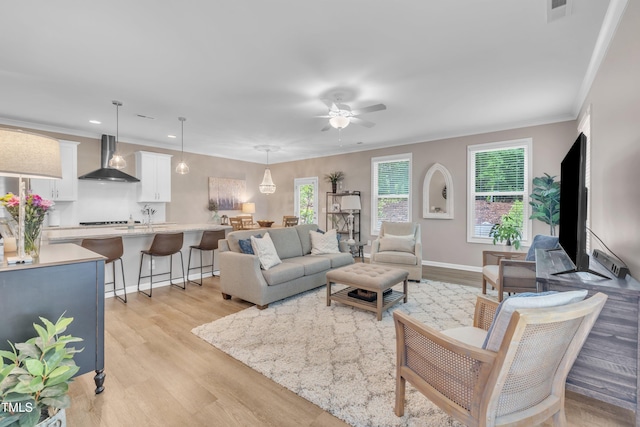 living area with light wood finished floors, ceiling fan, recessed lighting, ornamental molding, and baseboards