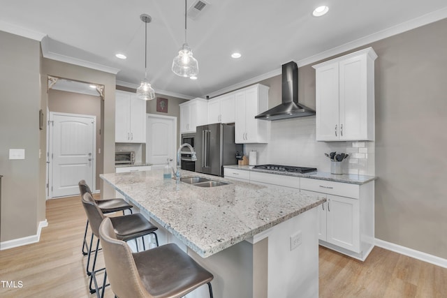 kitchen with wall chimney range hood, a sink, ornamental molding, a kitchen bar, and stainless steel appliances