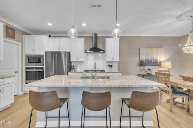 kitchen featuring wall chimney exhaust hood, stainless steel appliances, a sink, light wood-style floors, and a breakfast bar