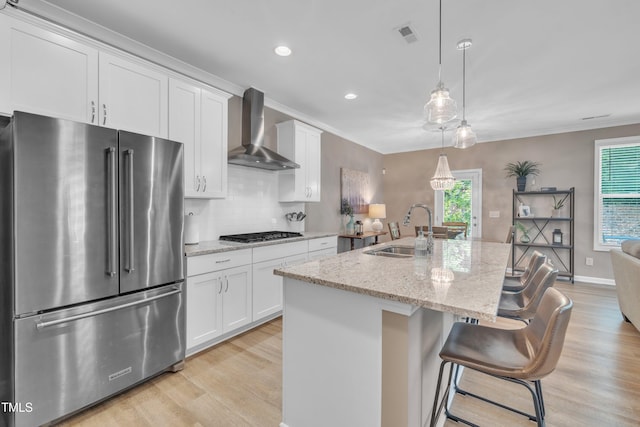 kitchen featuring stainless steel appliances, wall chimney range hood, a sink, ornamental molding, and light wood finished floors