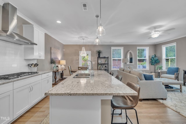 kitchen with a sink, wall chimney exhaust hood, stainless steel gas cooktop, light wood-style flooring, and crown molding