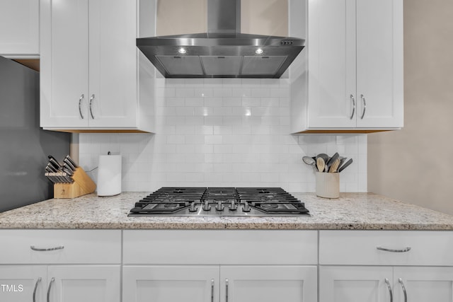 kitchen featuring wall chimney exhaust hood, stainless steel gas stovetop, white cabinets, decorative backsplash, and light stone countertops