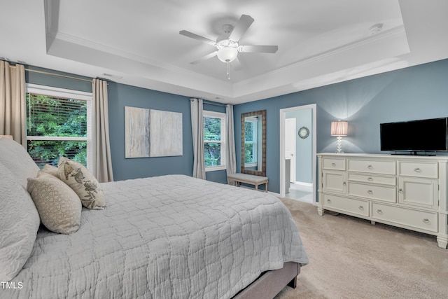 bedroom with a tray ceiling, crown molding, multiple windows, light carpet, and a ceiling fan