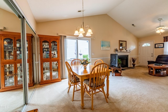 dining space featuring light colored carpet, a fireplace, a chandelier, high vaulted ceiling, and ceiling fan