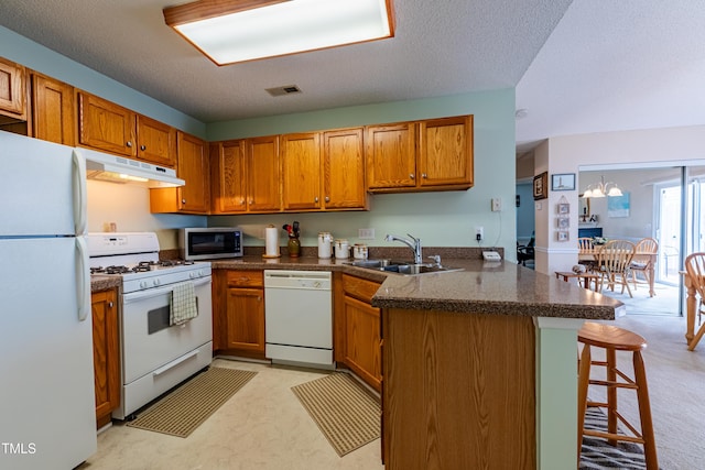 kitchen with white appliances, under cabinet range hood, a sink, brown cabinetry, and a peninsula