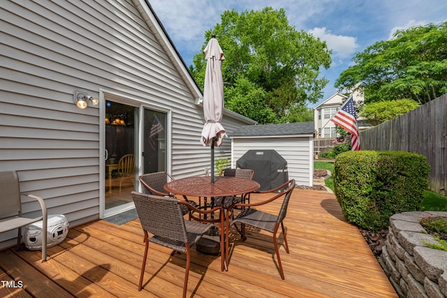 deck with outdoor dining area, fence, area for grilling, a shed, and an outbuilding