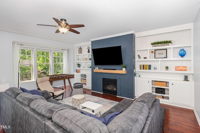 living area featuring dark wood-style flooring, a glass covered fireplace, ceiling fan, and built in features