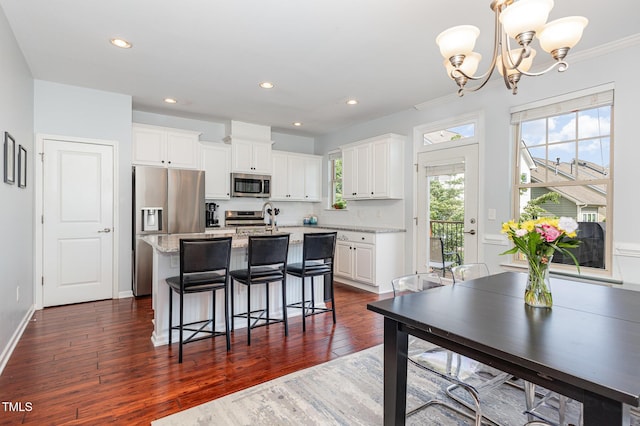 kitchen with appliances with stainless steel finishes, a kitchen island with sink, dark wood-style flooring, white cabinetry, and a chandelier