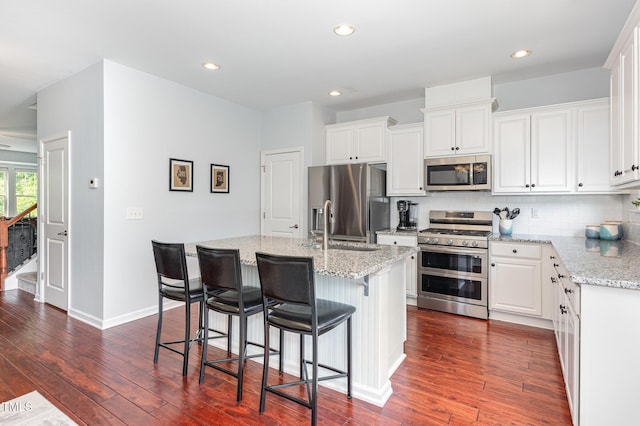 kitchen featuring appliances with stainless steel finishes, a sink, dark wood-style flooring, tasteful backsplash, and light stone counters