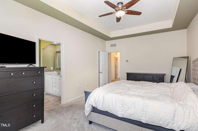 bedroom featuring light carpet, ensuite bathroom, baseboards, a raised ceiling, and a ceiling fan
