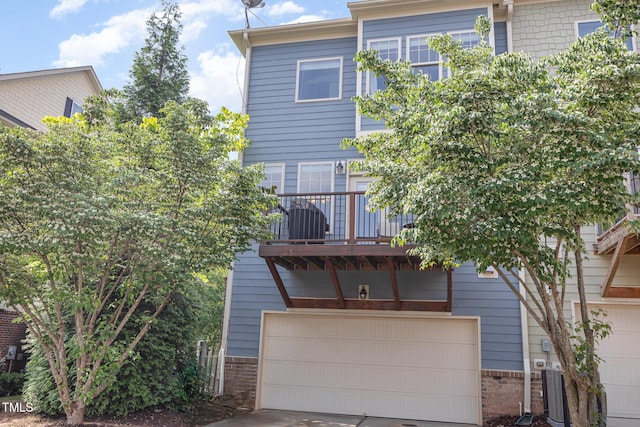 back of house featuring a balcony, a garage, brick siding, central air condition unit, and concrete driveway