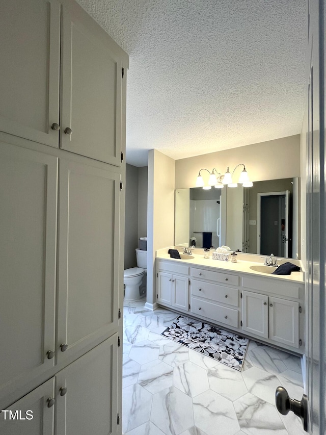 bathroom with toilet, marble finish flooring, double vanity, and a textured ceiling