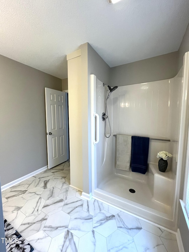full bath featuring marble look tiles, a shower, baseboards, and a textured ceiling