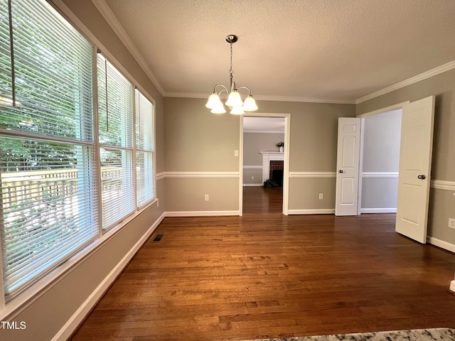 unfurnished dining area with a chandelier, a textured ceiling, dark wood finished floors, crown molding, and baseboards