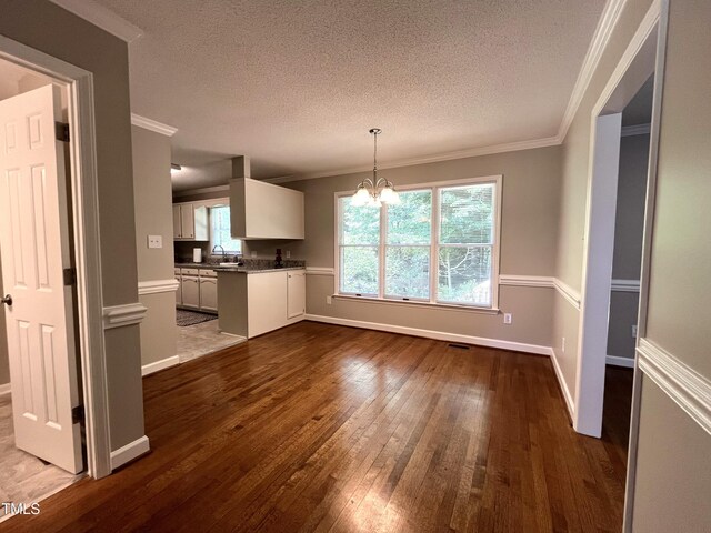 kitchen featuring a chandelier, dark wood-style floors, white cabinetry, a textured ceiling, and ornamental molding