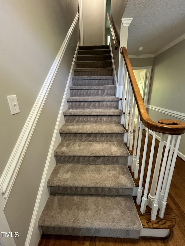 stairs with wood finished floors, crown molding, and a textured ceiling