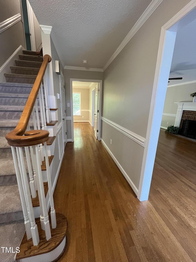 hallway featuring stairs, a textured ceiling, wood finished floors, crown molding, and baseboards