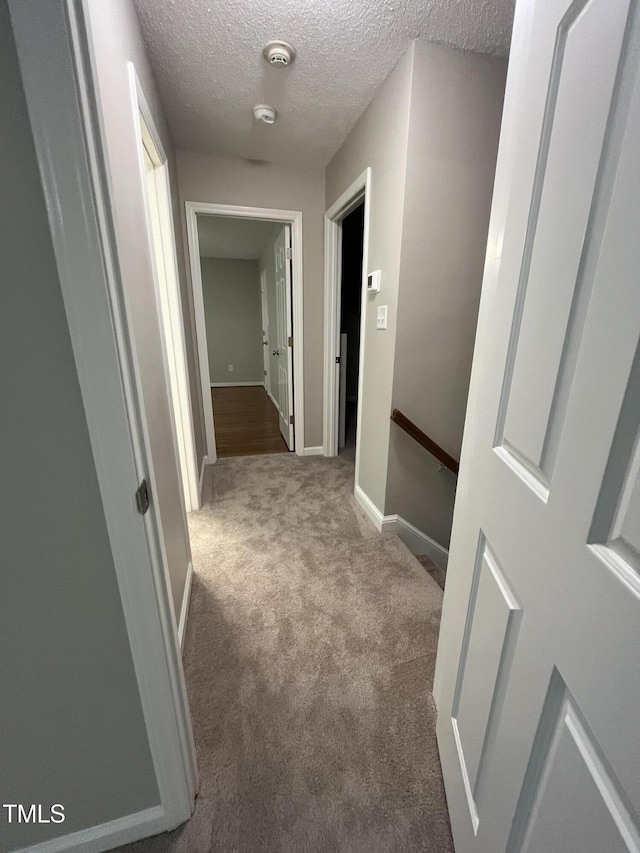 corridor featuring carpet floors, an upstairs landing, a textured ceiling, and baseboards