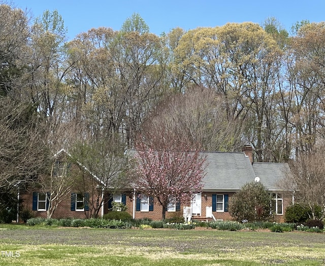 view of front facade featuring brick siding, a chimney, and a front yard