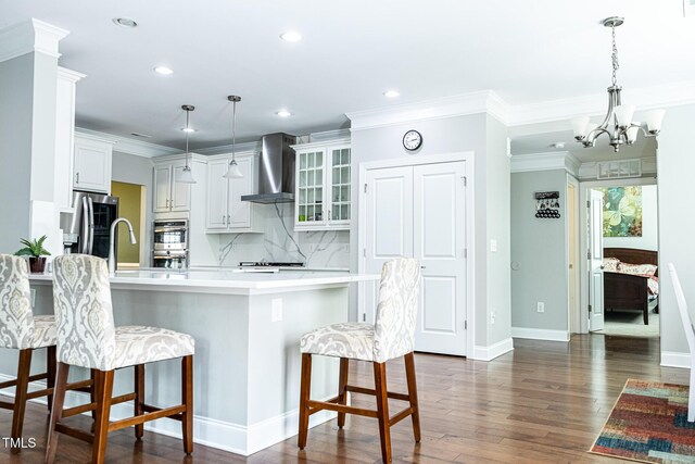 kitchen featuring wall chimney range hood, appliances with stainless steel finishes, a peninsula, a kitchen bar, and glass insert cabinets