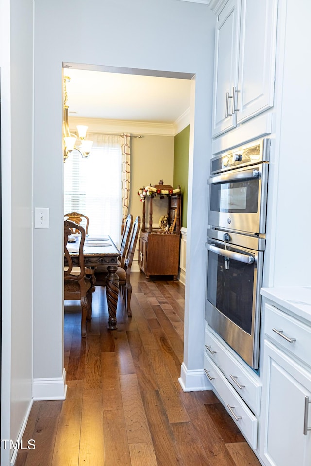 kitchen featuring double oven, dark wood-style floors, a chandelier, crown molding, and white cabinetry