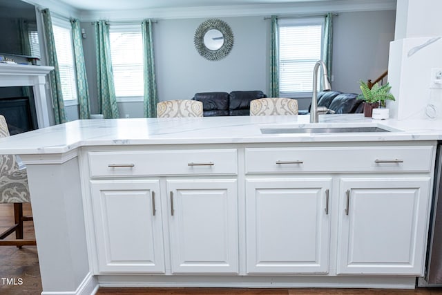 kitchen with a sink, ornamental molding, white cabinets, open floor plan, and light stone countertops