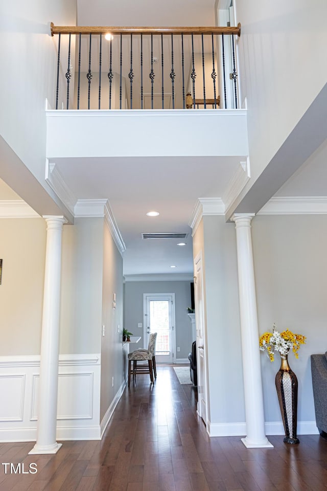 hallway featuring ornate columns, ornamental molding, dark wood-style floors, baseboards, and a high ceiling