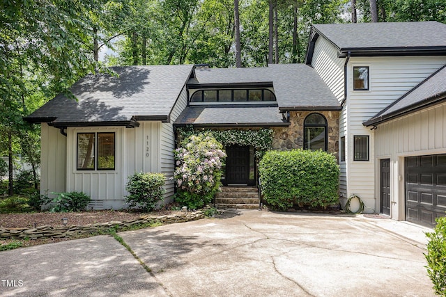 view of front of home with driveway, roof with shingles, board and batten siding, and stone siding