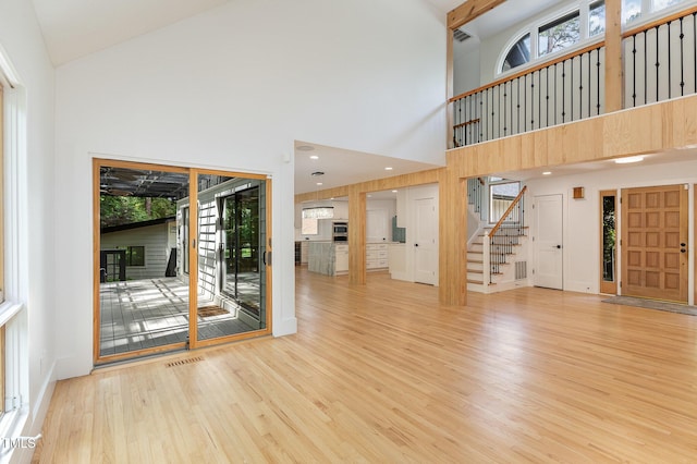 unfurnished living room featuring stairs, a towering ceiling, wood finished floors, and plenty of natural light