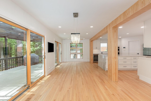 unfurnished living room featuring beverage cooler, light wood finished floors, a chandelier, recessed lighting, and baseboards