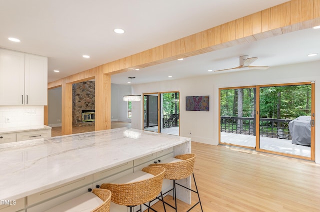 kitchen featuring a kitchen bar, light stone counters, white cabinets, light wood-style floors, and recessed lighting
