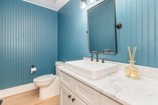 half bath with wood finished floors, crown molding, vanity, and toilet