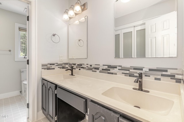 full bathroom featuring toilet, double vanity, backsplash, and baseboards