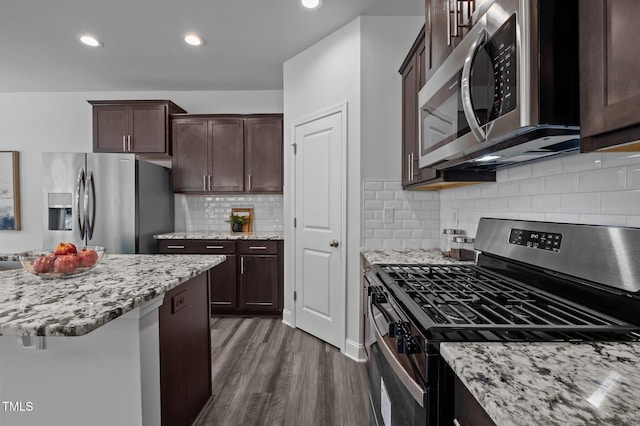 kitchen with appliances with stainless steel finishes, dark wood-style flooring, dark brown cabinetry, light stone counters, and backsplash