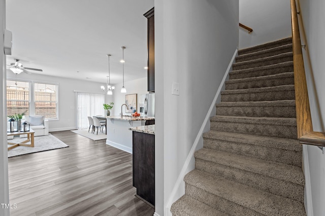 stairway with wood finished floors, a ceiling fan, a chandelier, and baseboards