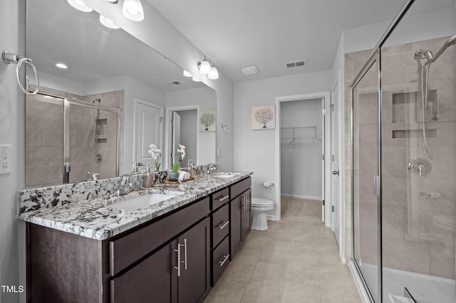 bathroom with a stall shower, double vanity, a spacious closet, toilet, and tile patterned floors