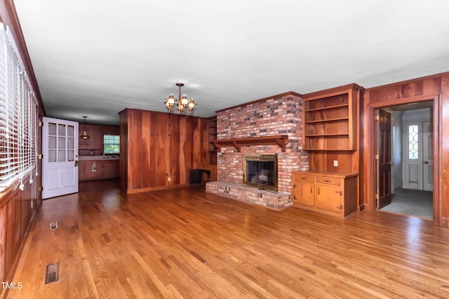411 W Killiegrey St, Lillington, NC 27546 - unfurnished living room with light wood-type flooring, a chandelier, wooden walls, and a brick fireplace