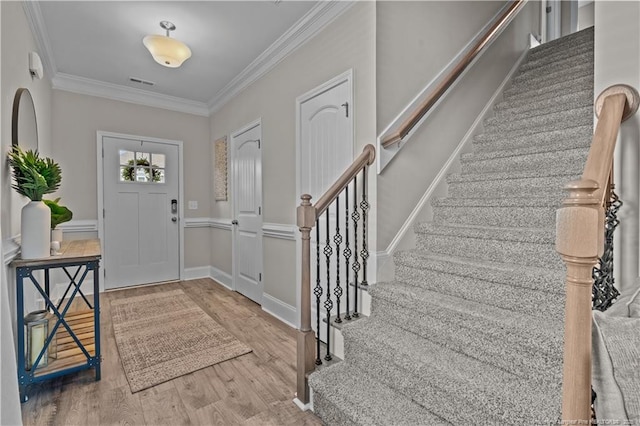 foyer entrance with stairway, crown molding, and wood finished floors