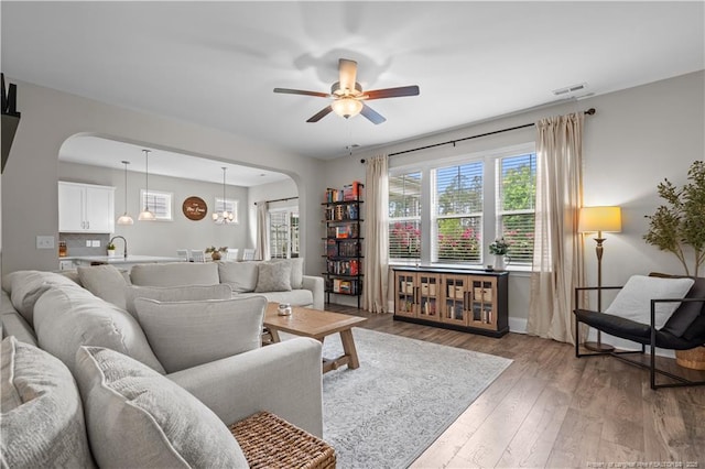 living room with arched walkways, ceiling fan, light wood-style flooring, and baseboards
